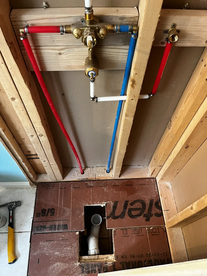 New shower valve body with fresh red and blue PEX supply lines and the drain below