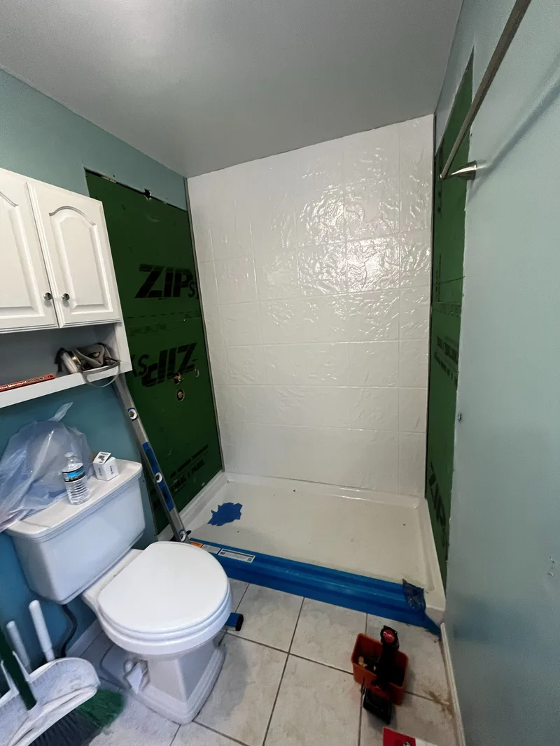 Shower with the back wall panelled, side walls still open, toilet still in place in the room
