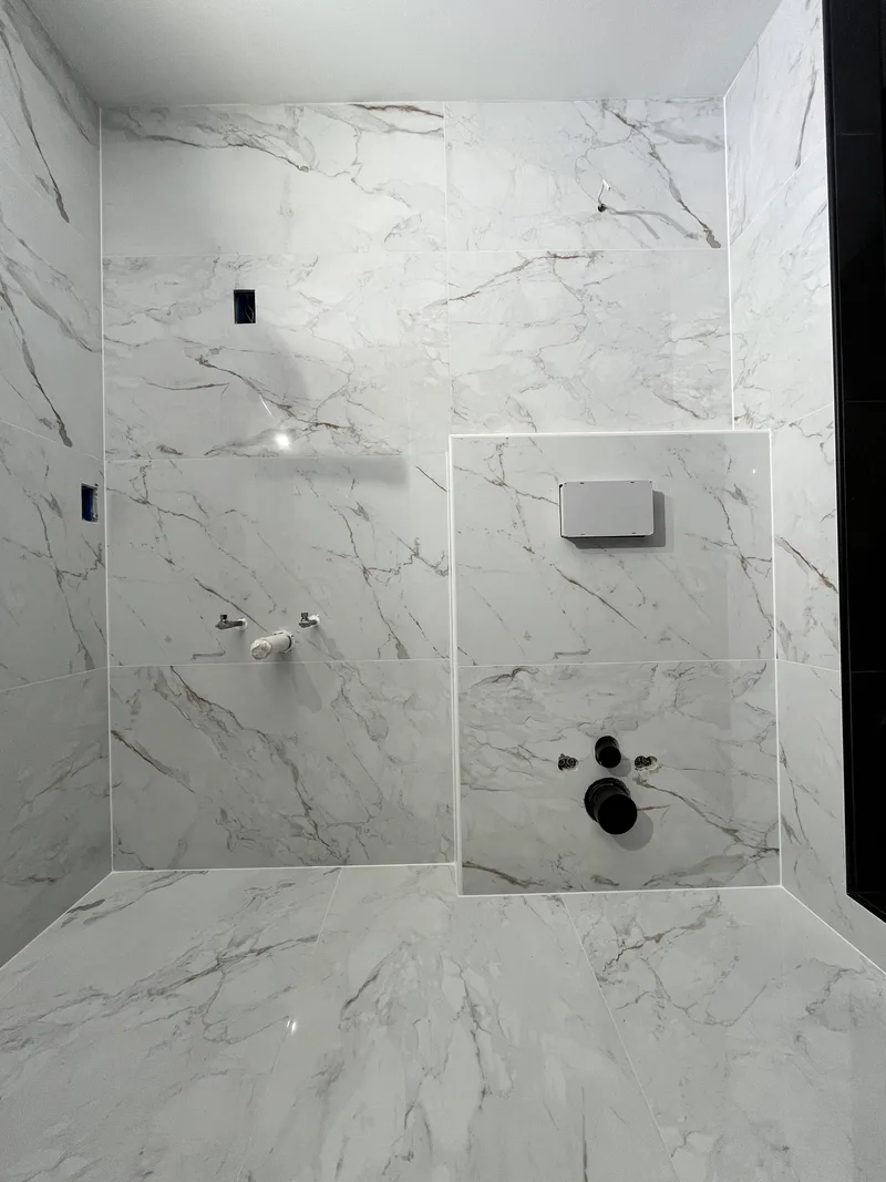 Full wall of large-format marble-look porcelain with 1/16 inch joints and the tiled access panel framed in