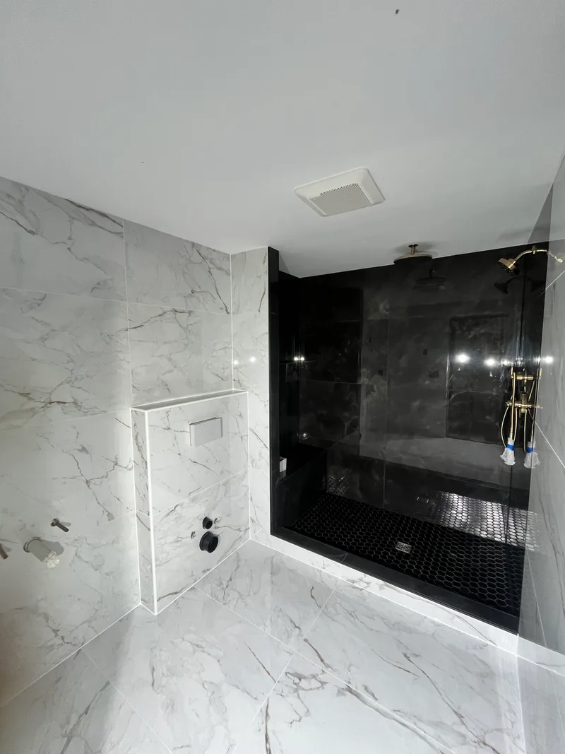 Finished Natick shower — black large-format porcelain and hex mosaic pan inside, marble-look walls out, mitered knee-wall cap with no metal trim