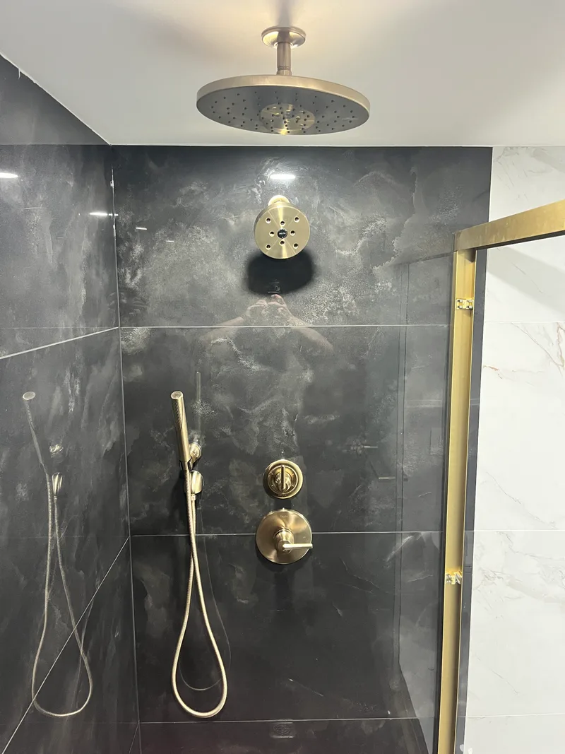 Brushed brass shower trim and diverter valve mounted on black large-format porcelain