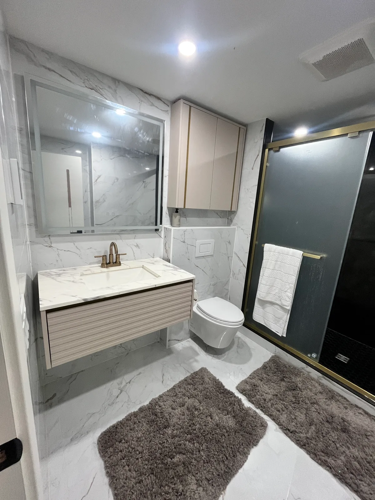 Bathroom remodeled by Queenstone Homes in Natick MA — large-format porcelain, wall-hung vanity and toilet, glass shower