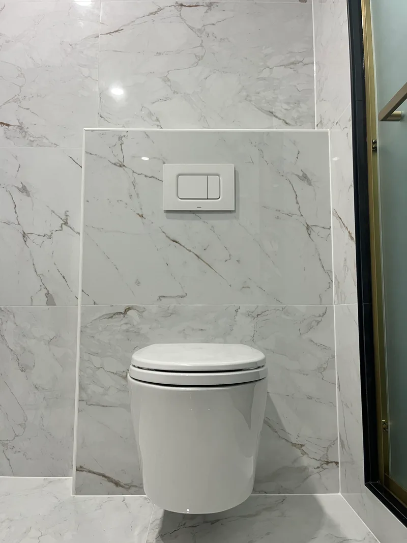 Wall-hung toilet with a concealed tank and a flush plate set into large-format marble-look tile