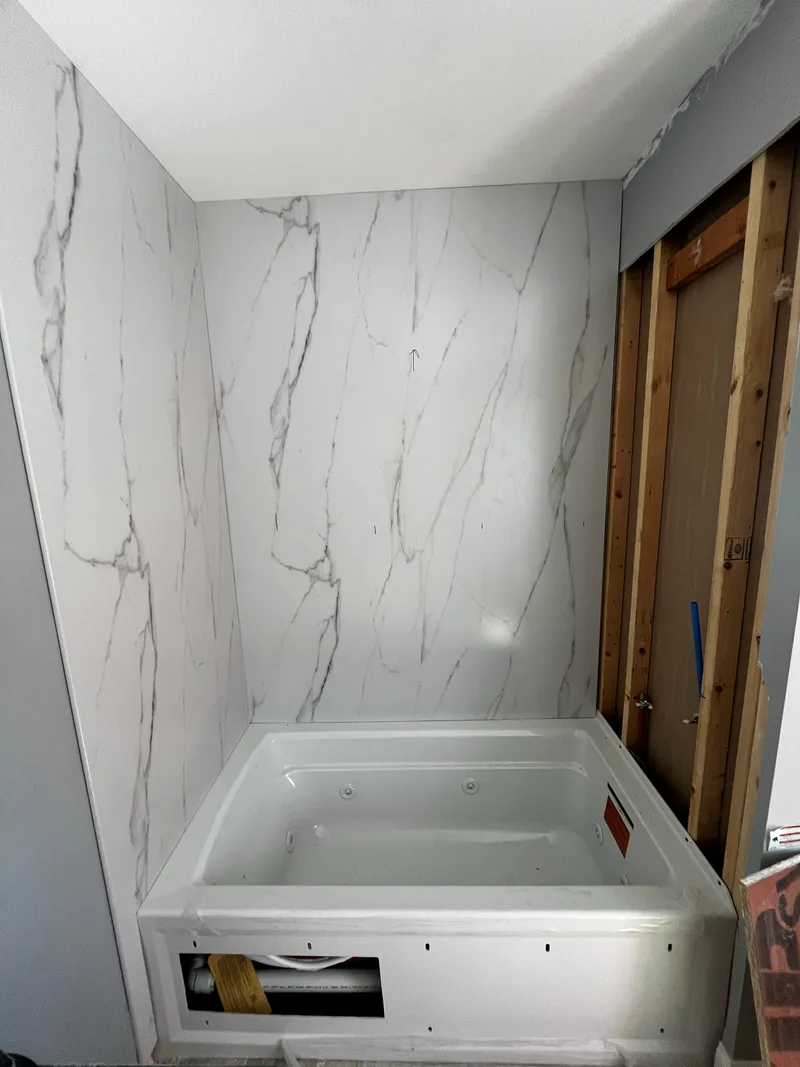 Two walls of the tub surround clad in marble-look composite panel